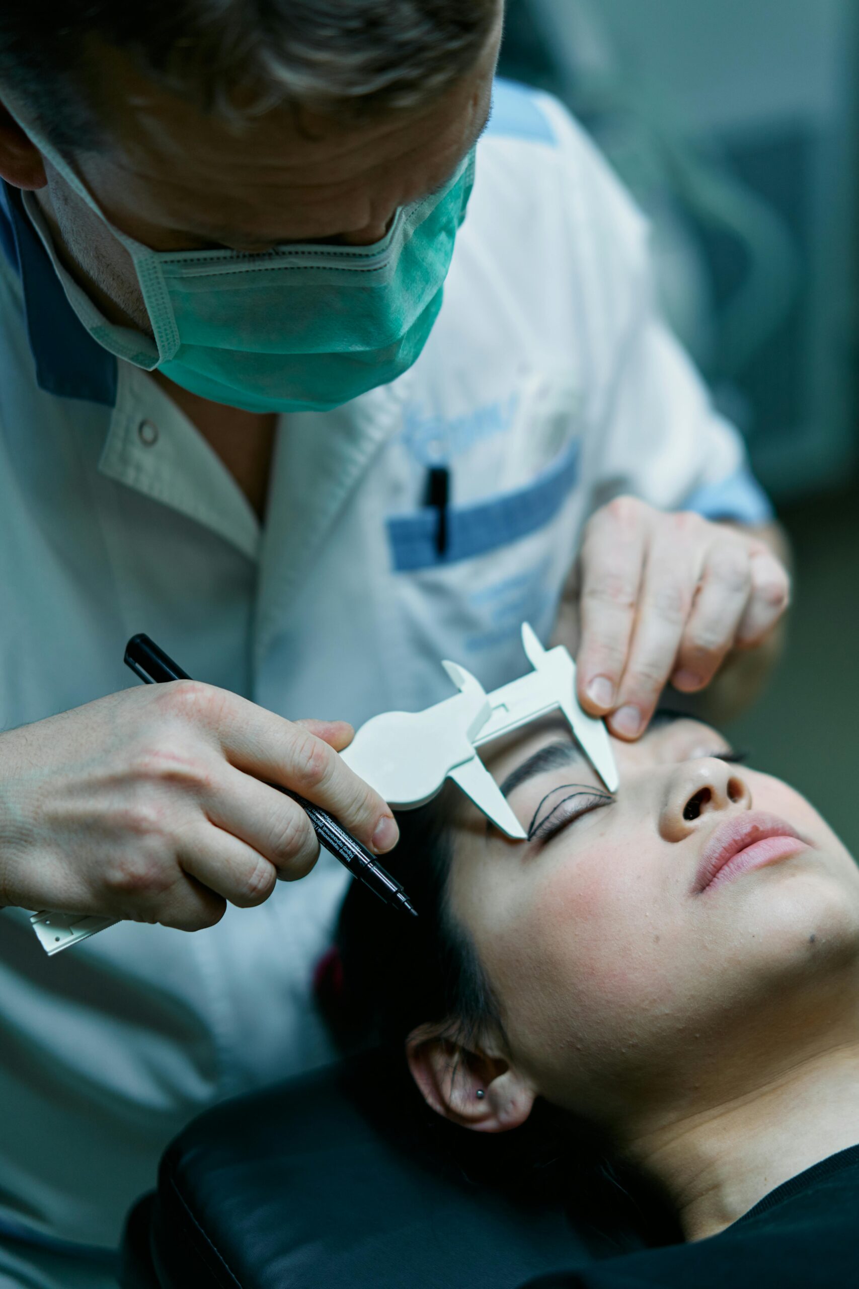 Surgeon measuring patient's eyelid before cosmetic surgery in medical clinic setting.